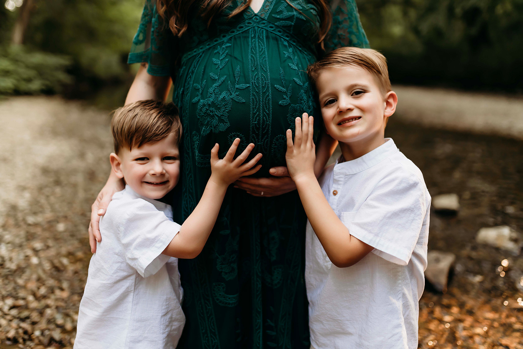 A pregnant women with her two sons on either side of her pregnant belly smiling.
