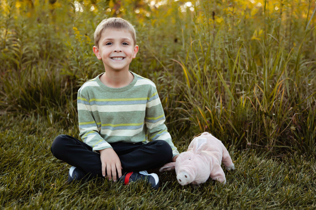 A little boy and his stuffed pig are sitting together for a picture.