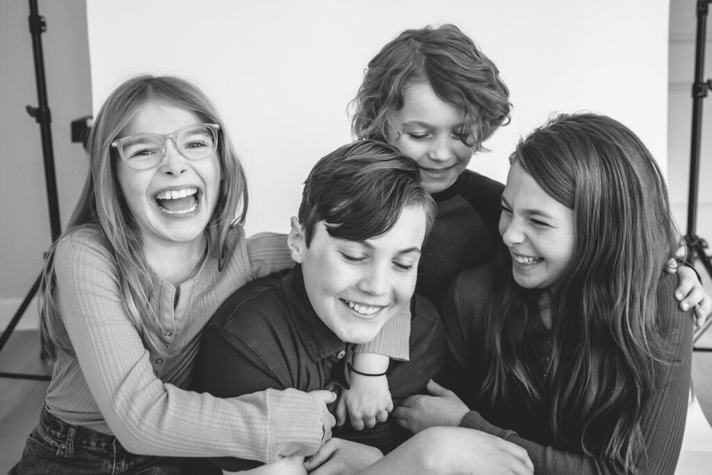 2 boys and 2 girls are hugging and tickling each other. They are laughing at their mini session. 