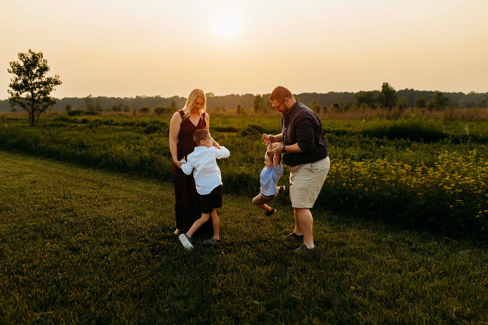 A mom is dancing with her son while the dad is swinging the other son. 