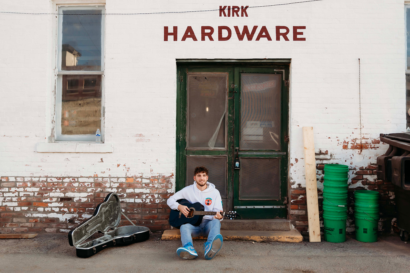 A boy sitting in a alley playing his guitar for a senior session.