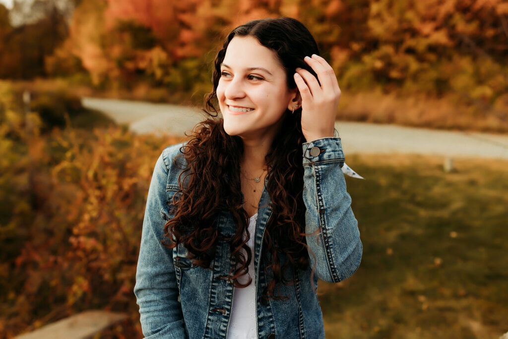 A girl wearing a jean jacket, looking to the side and smiling.