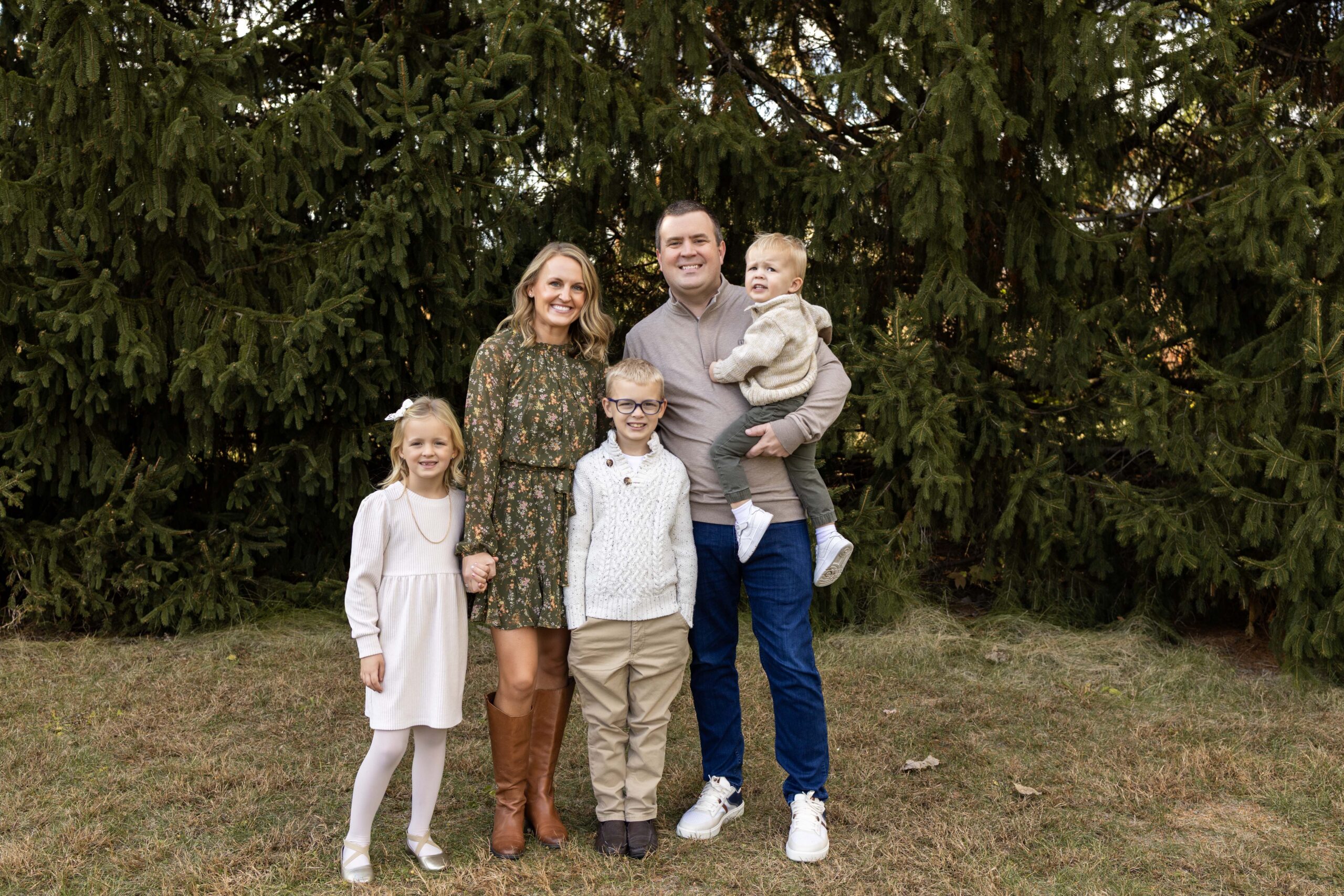 Family of 5 wearing greens and cream standing close together smiling for a family photo with noblesville family photographer.