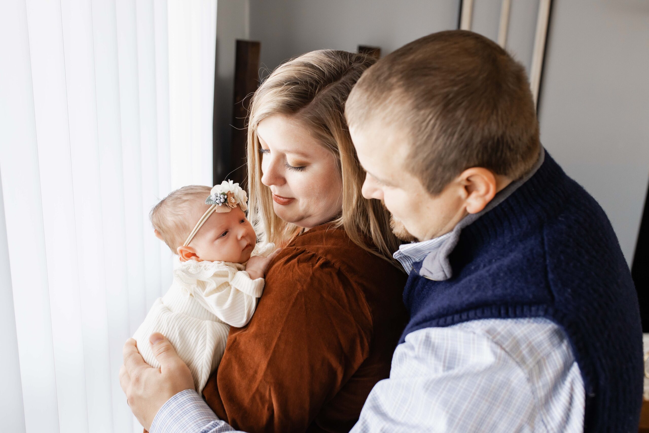 A mother holding her newborn over her shoulder with dad close behind smiling at the baby. Carmel newborn photographer