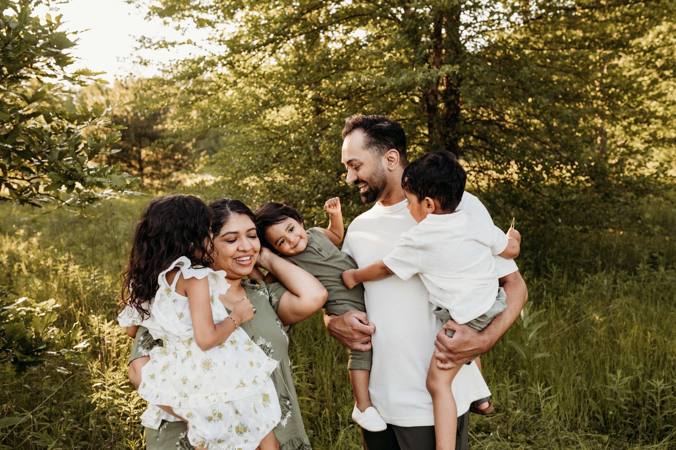 A mom and dad holding all three little kids. Tickling each other and laughing. Carmel family photographer