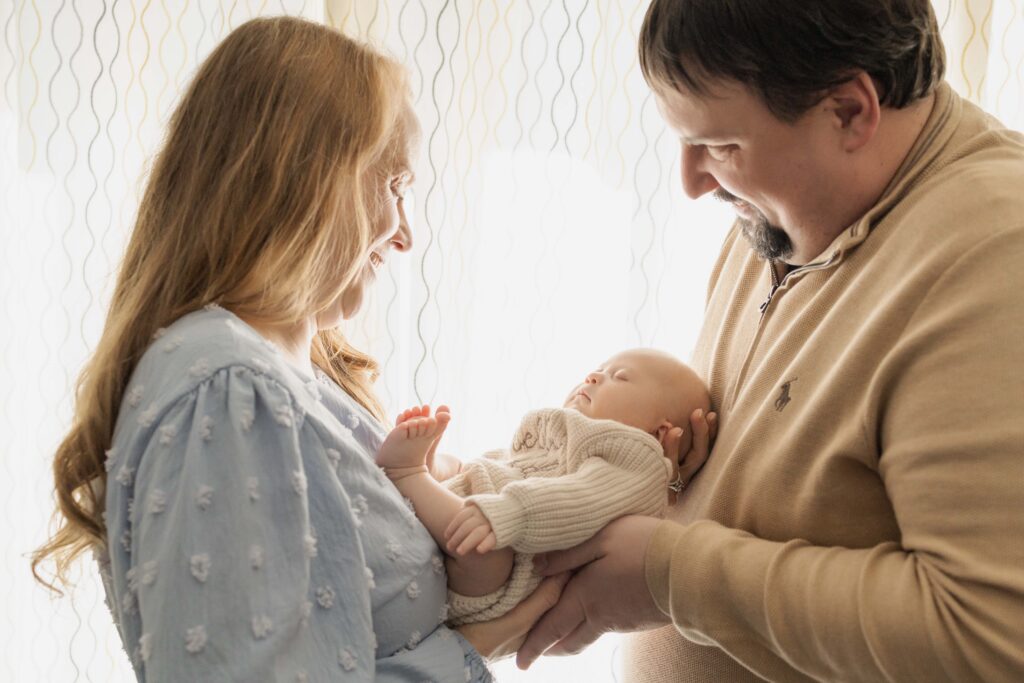 Mom and Dad are facing each other with their newborn baby in between them. Indianapolis newborn session.