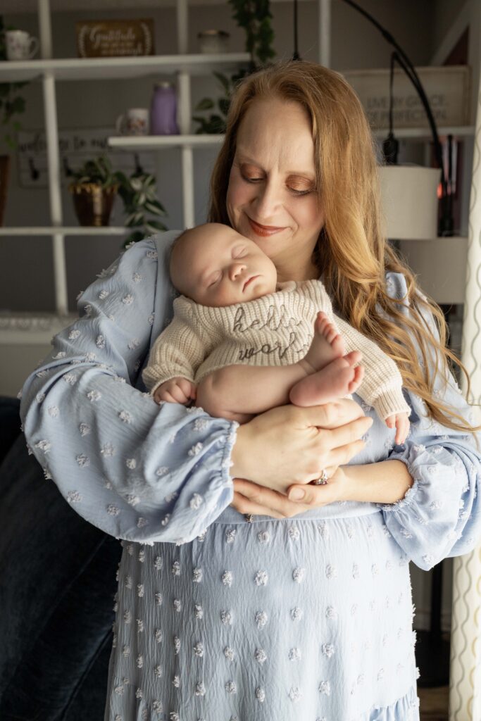 A mom holding her newborn baby close to a window and smiling down at him. Indianapolis newborn session.