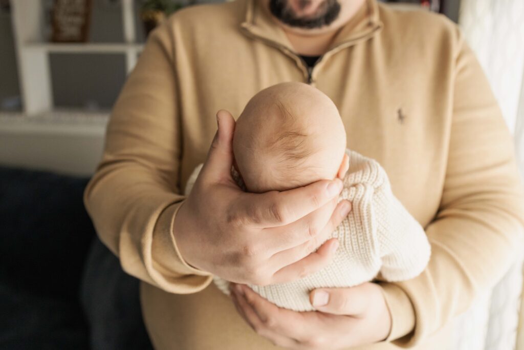 A close-up of dad holding a newborn baby, showing how big his hands are compared to his tiny son.