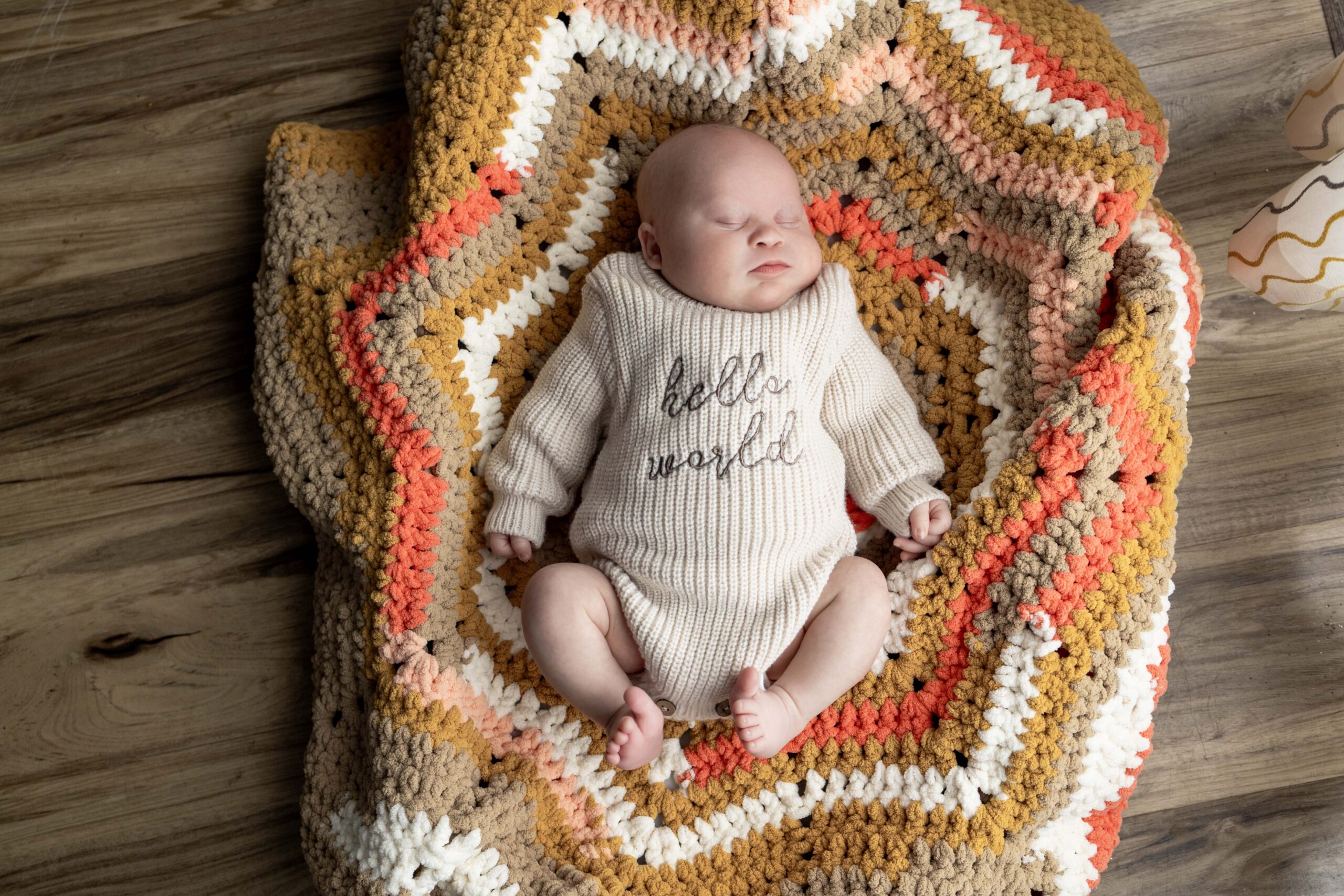 A squishy newborn baby lying in a baby basket with a knit blanket under him.