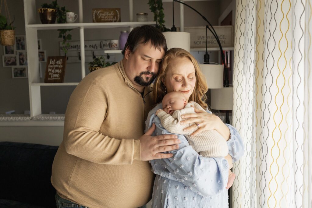 A mom is holding her new baby boy up on her shoulder, and Dad is coming in from behind for a hug. Indianapolis newborn photographer.