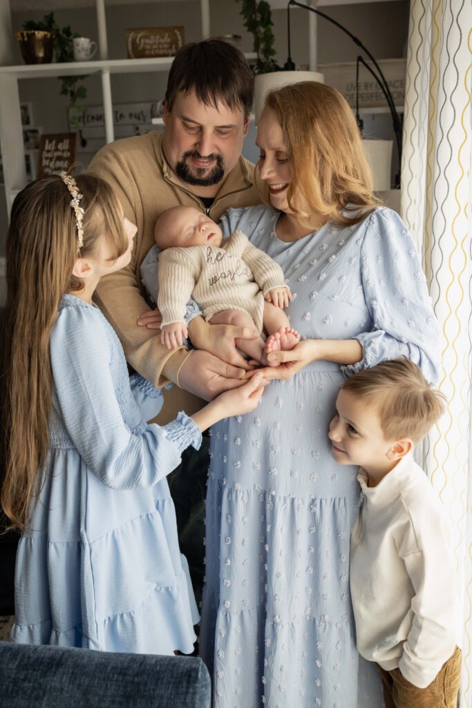 A mom holding her newborn with her husband and older son and daughter all snuggling close to her. Indianapolis newborn session.