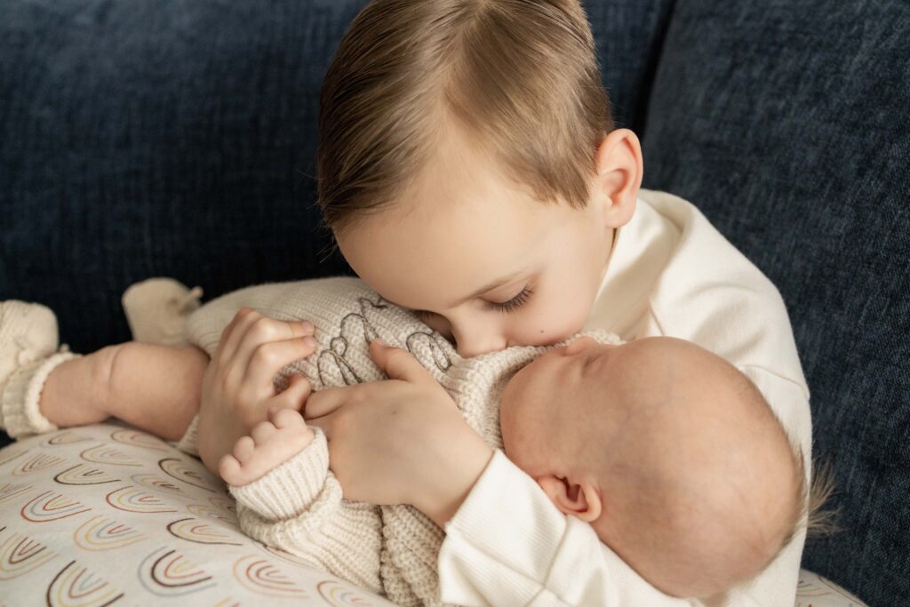 A big brother holding his newborn brother and giving him kisses.