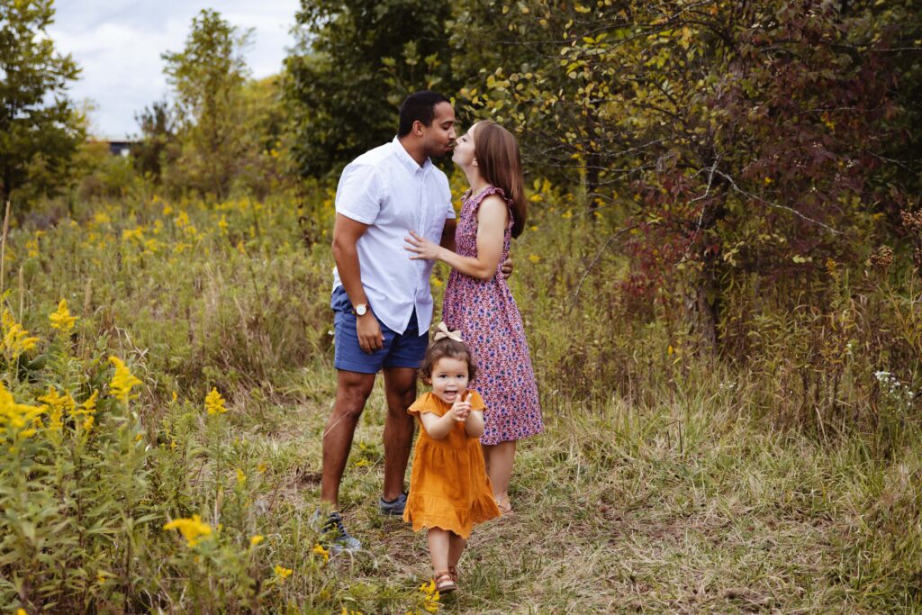 Mom and Dad kissing with a toddler running around. Westfield family photographer.
