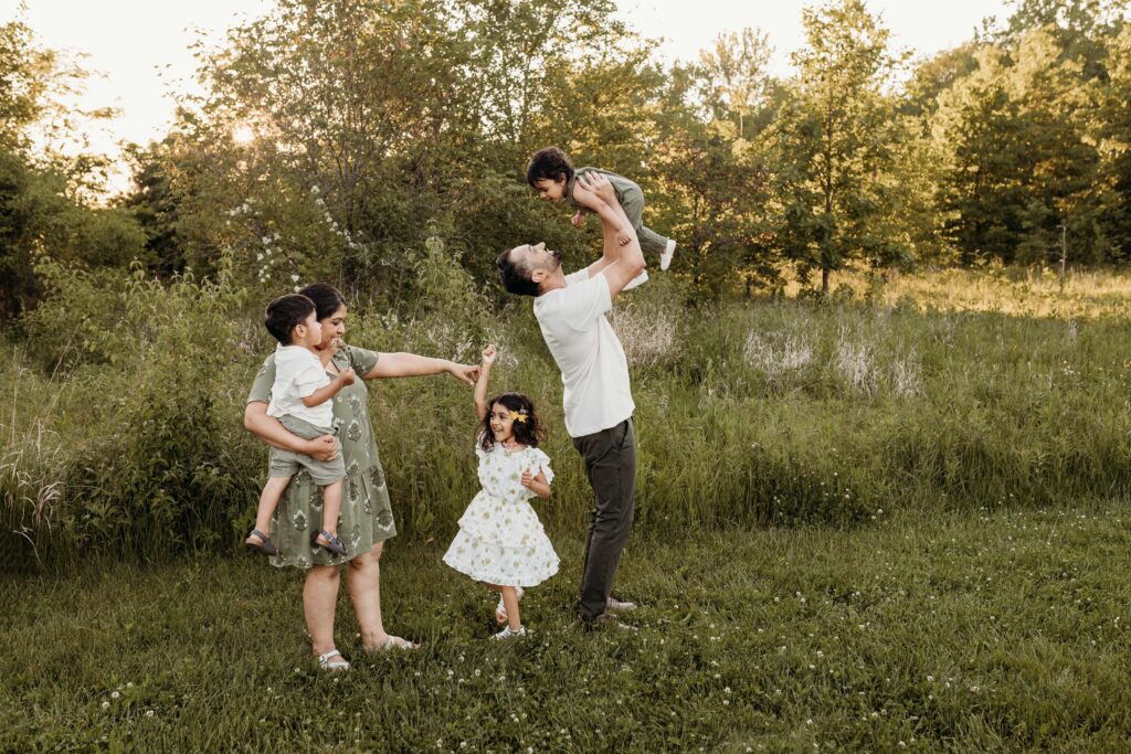 A mom and dad with 3 kids playing in a field, dancing and laughing. Carmel family photographer. 
