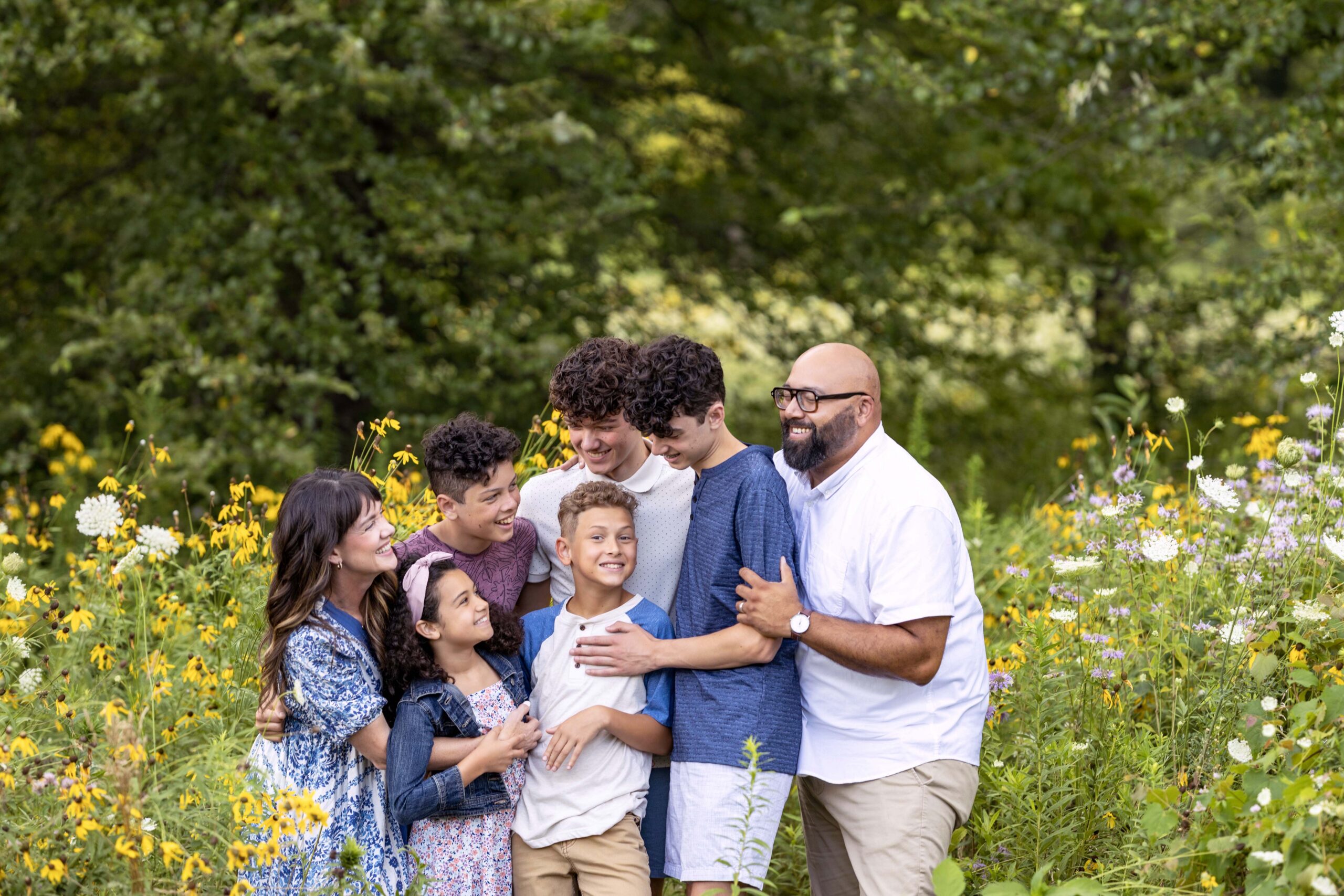 A family of seven standing close together hugging among wildflowers. Indianapolis family photographer.