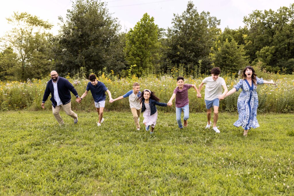 A family of seven all holding hands and running and smilling. Indianapolis family photographer
